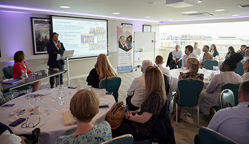 Prof Suvankar Pal standing at a lectern in a conference room, presenting to an audience seated around round tables